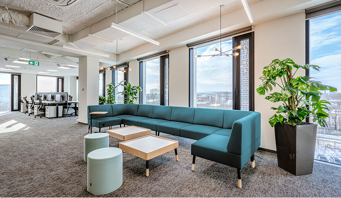 The Sprout Social office in Poland, showing a lounge with a sofa and tables, surrounded by large windows and plants.