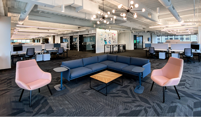 The Sprout Social office in Seattle, an open-plan space with a large L-shaped sofa, two armchairs‌ and a wooden table.